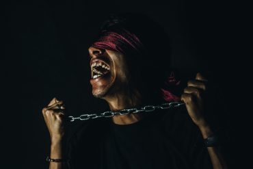 "Corporate Idolatry" by Helena Hawkins - blindfolded person trying to break free from chains